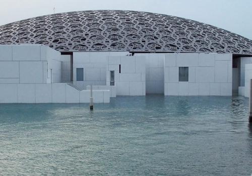 В парке музея Лувр Абу-Даби посетители любуются тем, как прямоугольные галереи и резной купол соприкасаются с водой и небом
